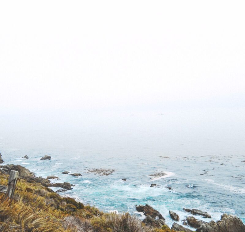 Eine Steile Küste mit Wellen die sich an Felsen brechen, das Meer liegt in weißem Dunst