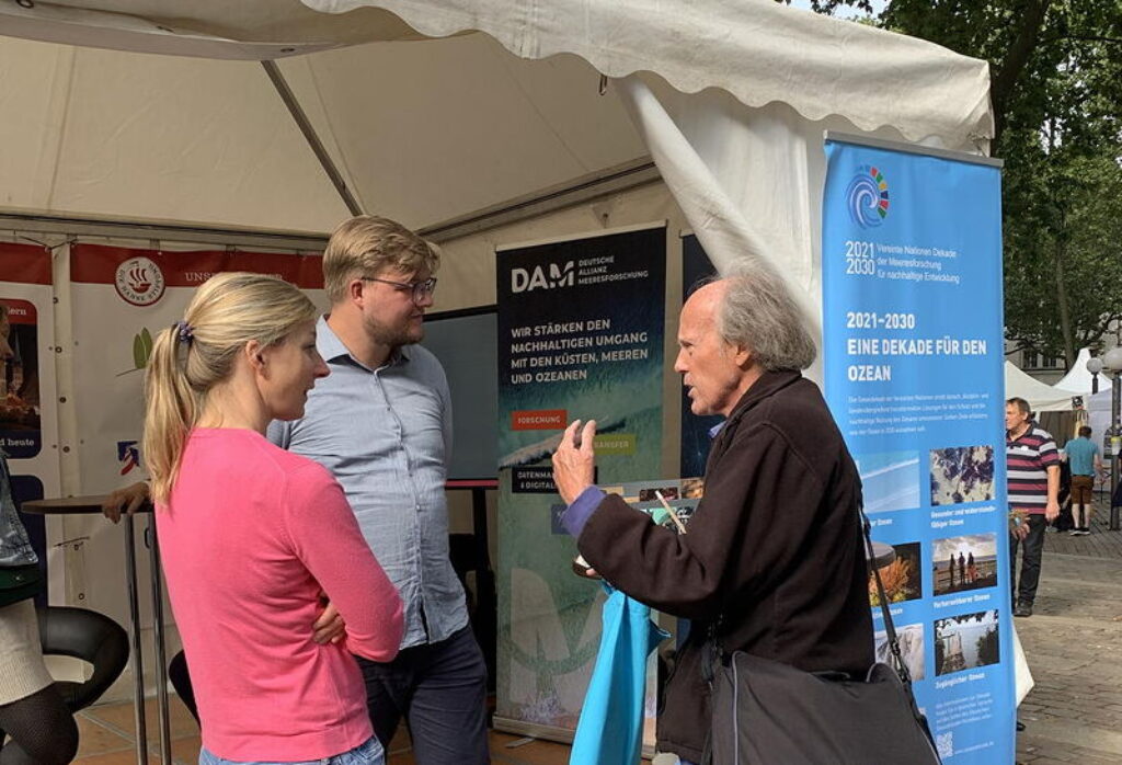 Menschen diskutieren am Stand der DAM zum Deutschlandtag am 3. Oktober 23 in Hamburg