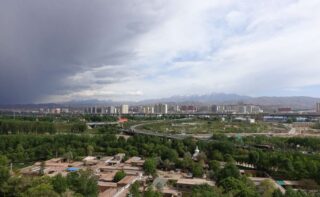 zentralasiatische Großstadt und Autobahn, im Hintergrund Berge, trübes Wetter
