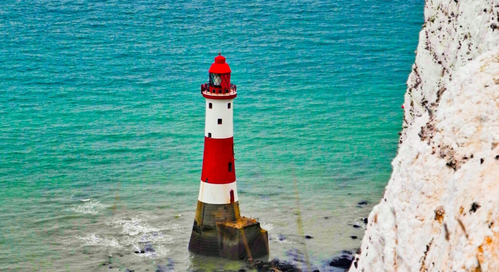 Weiß-roter Leuchtturm vor Kreidefelsen im Wasser