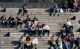 Menschen sitzen in kleinen Gruppen auf einer breiten Treppe