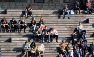Menschen sitzen in kleinen Gruppen auf einer breiten Treppe
