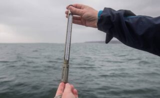 Karen Helen Wiltshire hält ein Termometer. An der "Helgoländer Straße" läuft seit 1962 täglich die detaillierteste Langzeitüberwachung des Meeres. Seit fast 60 Jahren kämpft sich jeden Tag ein kleines Forschungsschiff aus dem Hafen auf Helgoland in die offene Nordsee. In den vergangenen 60 Jahren betrug die durchschnittliche Erwärmung des Wassers an der Helgoländer Straße 1,9°C, was etwa dem Doppelten der Erwärmung des globalen Ozeans entspricht.